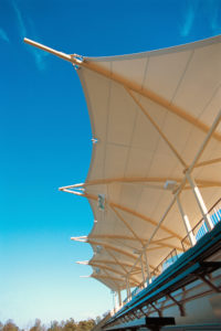 The Avery Aquatic Center at Stanford University features a pair of tensile canopies that face each other, arching over the bleacher seating for the diving pool. Scalloped-edged fabric forms are supported on arched steel ribs connected in pairs alternating open-front, open-back, like scissors. Photo: Huntington Design Associates Inc.