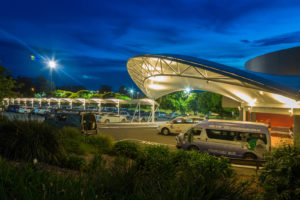 The curved triangular truss of the Wyong Rugby League Club porte cochère is held in place by two very large stainless steel pins at each end. Two curved rafters attached to a rolled universal beam placed against the building resist the outward rotation of the truss. In a neat trick of efficiency, the universal beam also acts as a rain gutter. Photo: Shade To Order Pty. Ltd.