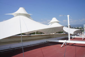 Above the roof, this view shows a latticework of supporting steel beams (painted white) where small masts and steel cables attach. The latticework evenly distributes loads across the existing roof. Note the smaller fabric top covers at the peaks. Photo: Courtesy Valarias DRV