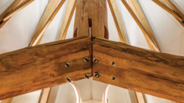 View of a wooden beam structure from below, showcasing angular wooden supports and a light, airy ceiling design.