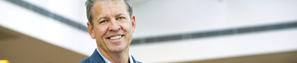Smiling man in a blue blazer against a bright, modern background with soft lighting, conveying a professional atmosphere.