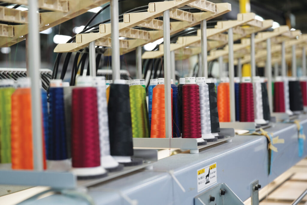 Colorful spools of thread in various shades, arranged in rows on a sewing machine setup in a factory environment.