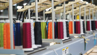 Colorful spools of thread in various shades, arranged in rows on a sewing machine setup in a factory environment.