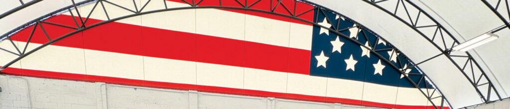 Red and white stripes with a blue field featuring white stars, framed by a curved black structure, set inside a bright, spacious interior.