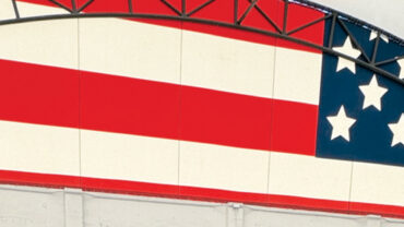 Red and white stripes with a blue field featuring white stars, framed by a curved black structure, set inside a bright, spacious interior.