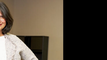 A woman with shoulder-length brown hair smiles confidently against a 'Liberty Awnings and Shades' banner, featuring red, white, and blue elements.