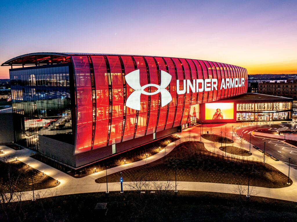 Striking red and glass Under Armour building at sunset, showcasing large logo and illuminated pathways in a modern outdoor environment.