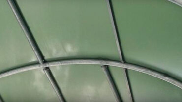 Green fabric canopy viewed from below, featuring curved metal supports and a smooth surface, creating a spacious overhead structure.