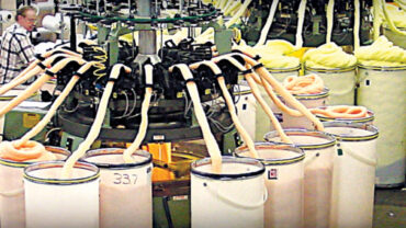 Manufacturing facility with spinning machinery and colorful spools; yellow, orange, and white materials arranged neatly, highlighting industrial processes.