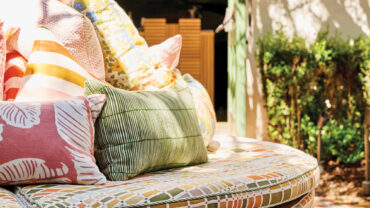 Colorful outdoor cushions in a patterned round seating area, with greenery and soft natural light creating a bright, inviting space.
