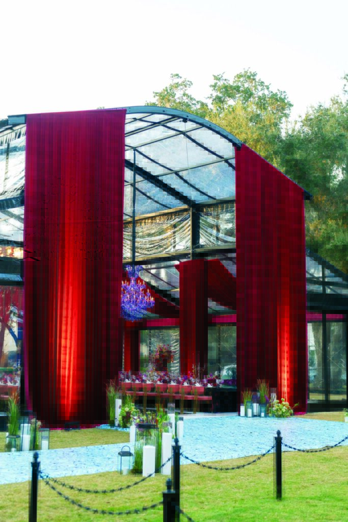 A luxurious outdoor wedding tent features rich red drapery and a sparkling chandelier, with elegant tables set for guests.