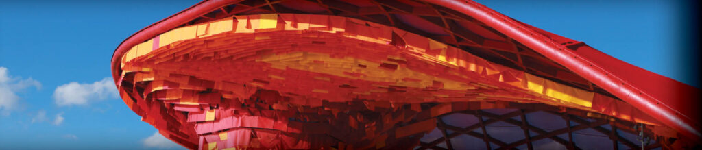 Architectural structure with a vibrant, red and yellow canopy, featuring intricate geometric patterns against a blue sky.