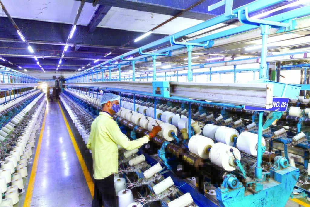 A textile worker operates machinery in a brightly lit factory, surrounded by rows of spools and clear blue overhead lighting.